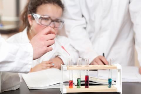 Image of students in lab coats and goggles filling test tubes with different coloured liquids