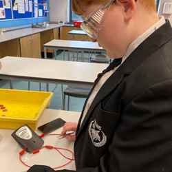 A boy wearing safety goggles conducts a battery experiment.