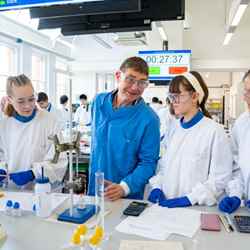 Dr Tony Raynham, UEL BSc chemistry course leader, stands in the middle of a group of four students conducting an experiment