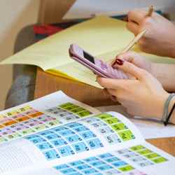 A student holds and works on a calculator while the periodic table lies on a table