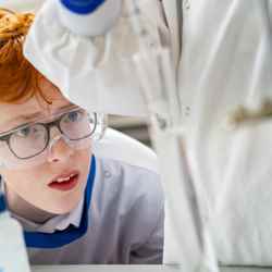 A redheaded student wearing safety goggles watches an experiment