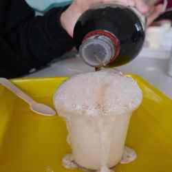 Coca-Cola is poured into a plastic cup, which is overflowing with foam