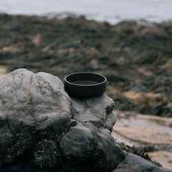 A little container lid made out of Notpla Rigid on a stony beach