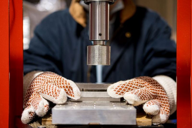 A pair of gloved hands works on a machine to produce Notpla Rigid
