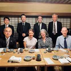 Two rows of four people sit and stand around a dinner table in Tokyo, Japan. The RSC's Sara Bosshart, Helen Pain and Anthony Galea sit second left, second right and right in the front row.