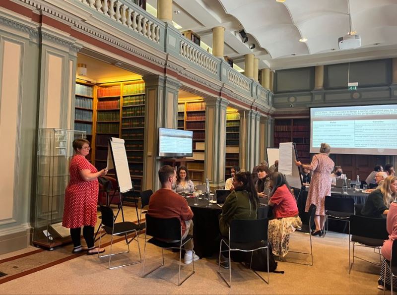 A landscape image of the Anxious Reactions event in Burlington House with attendees sitting at round tables and facing a screen at the back of the room