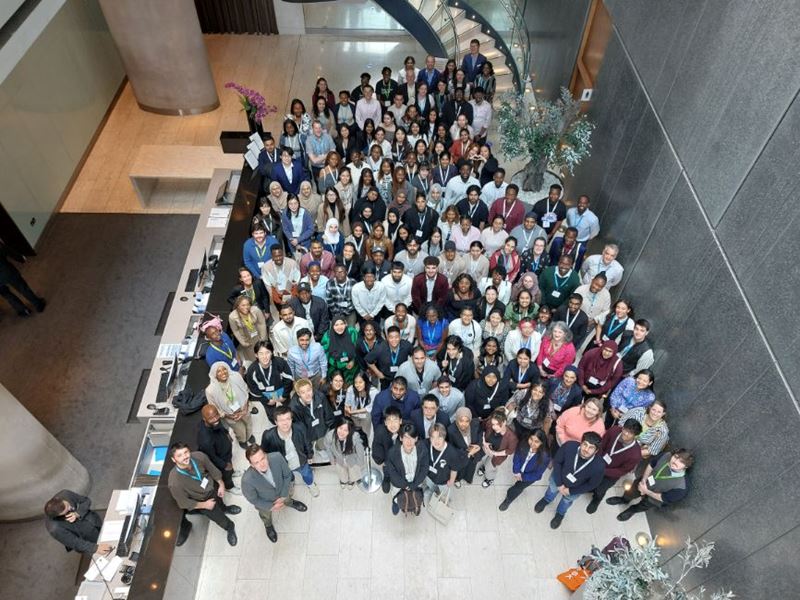 More than 100 young Black and minoritised ethnic chemical scientists, company representatives and RSC staff stand in the reception area of a hotel while looking up towards the camera and smiling