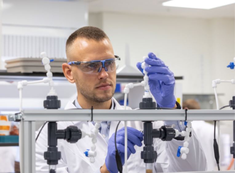 Henrik Hagemann, who is the Chief Executive Officer and Cofounder, wears safety glasses, a white coat and protective gloves as he works with equipment in the lab