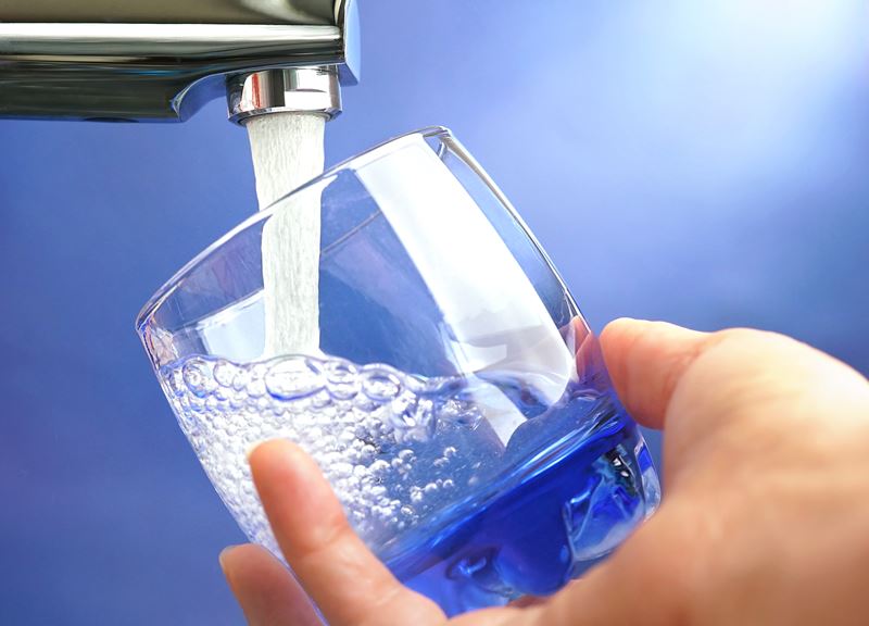 A hand holds a glass as a tap fills it with water